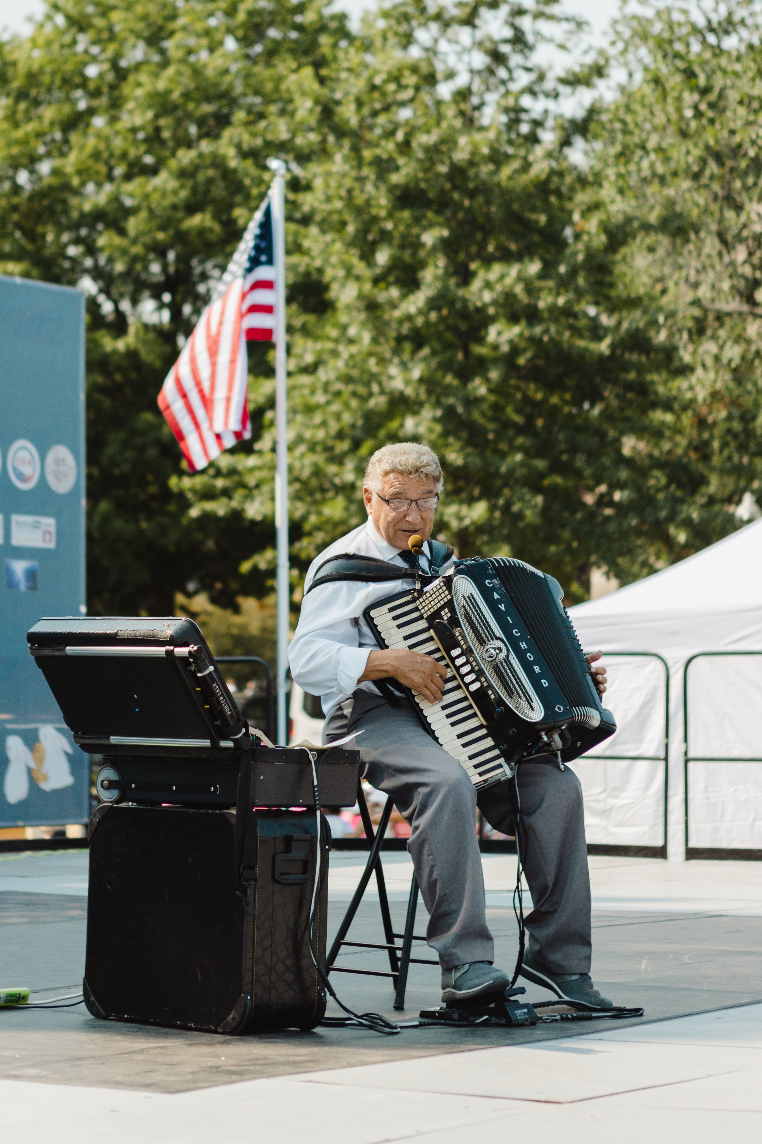 Musicians play accordions at an outdoor event with American flags in the background.