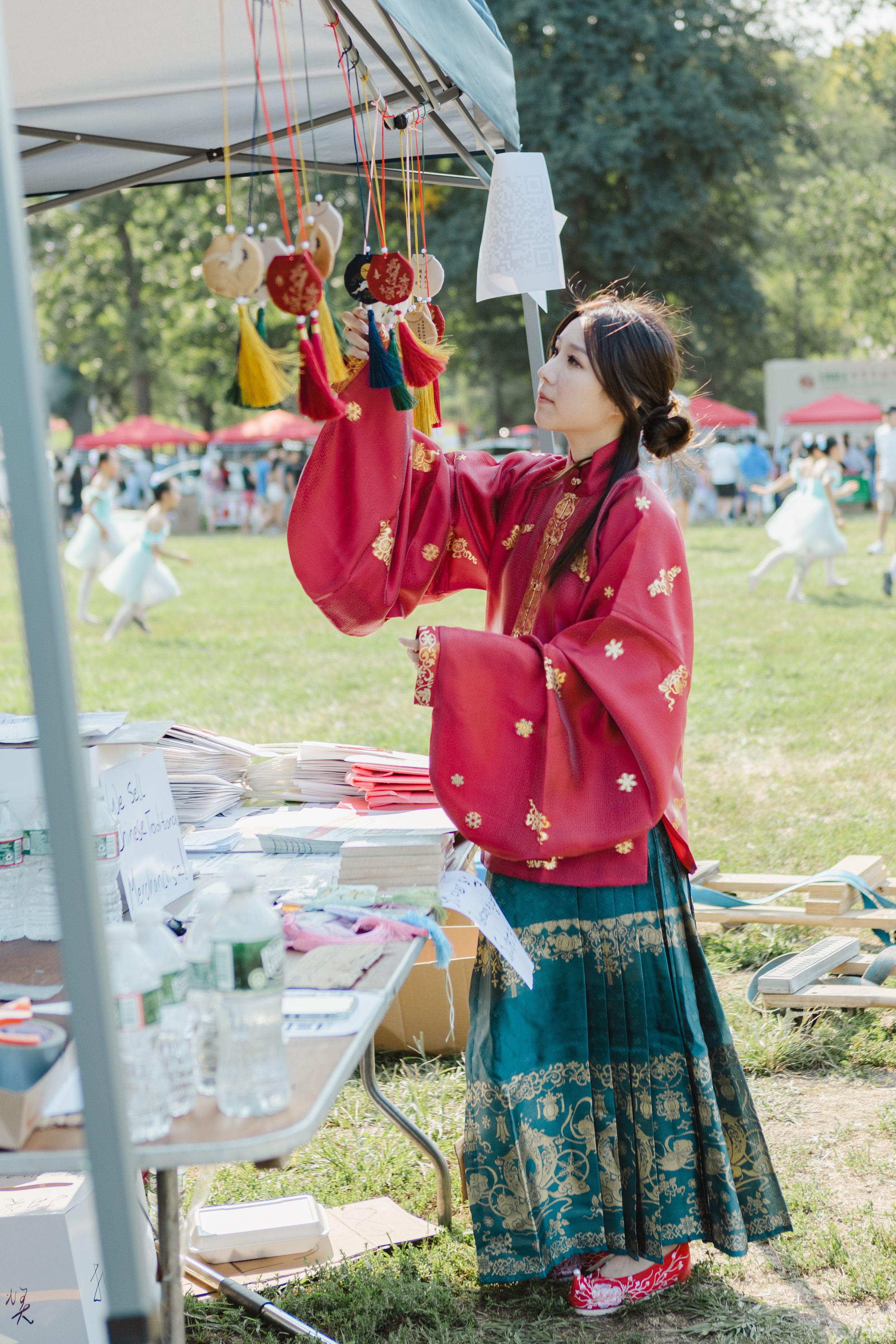 People in traditional red Asian clothing demonstrate puppet manipulation at an outdoor festival.
