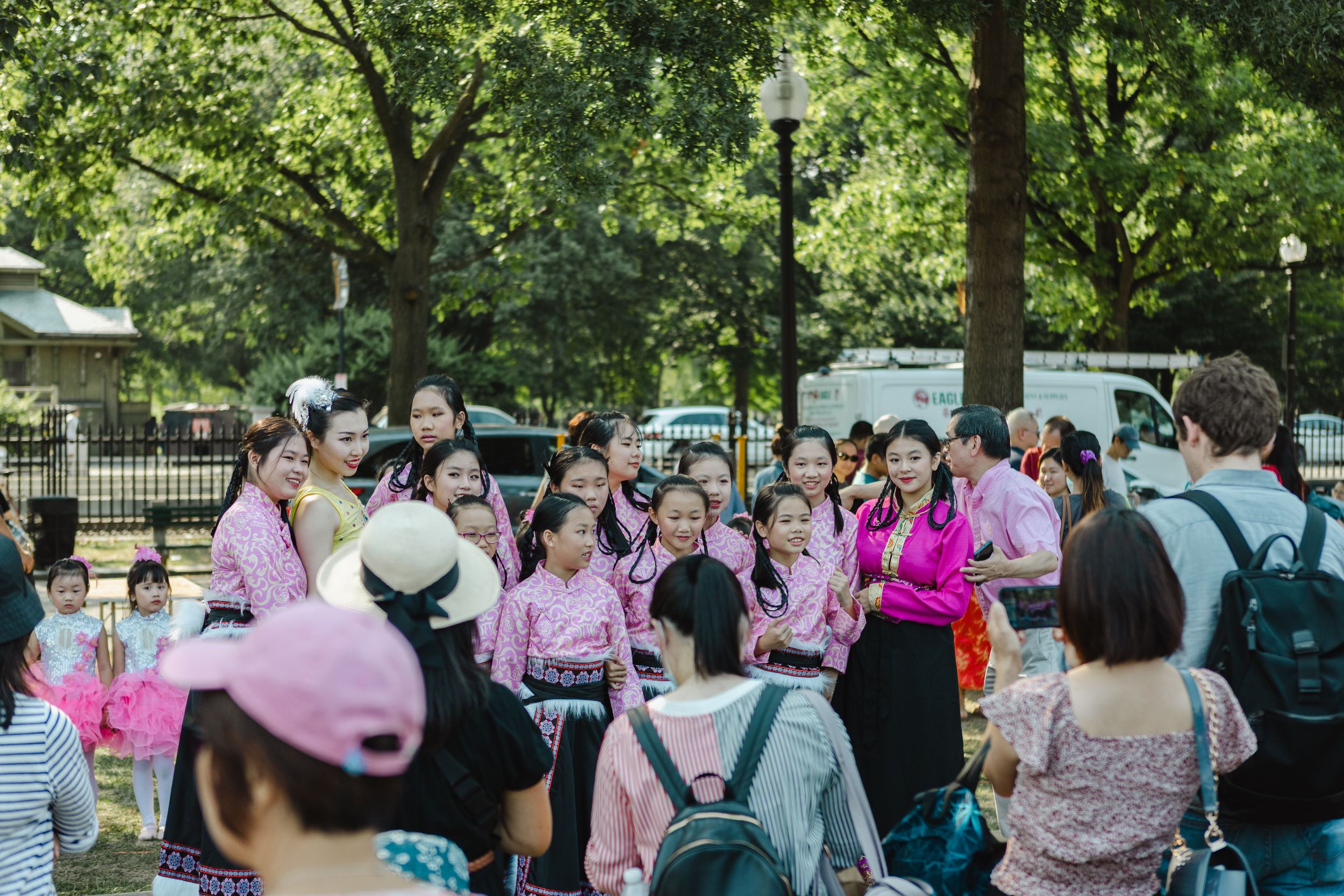 Crowd gathered at an outdoor festival event under green leafy trees.