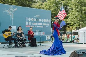Stage performance with musicians and dancers against blue backdrop and American flag.