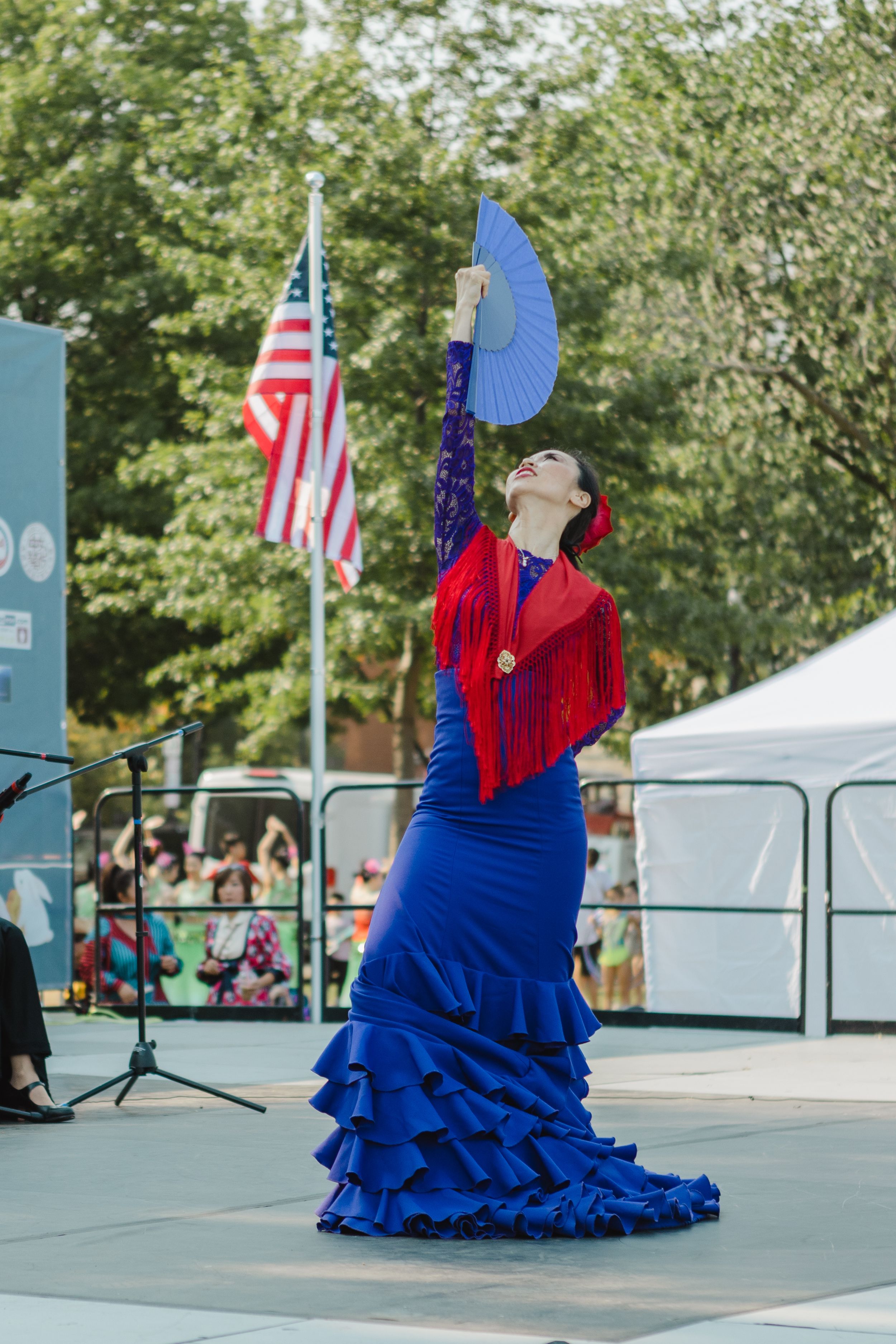 Flamenco dancer in flowing blue ruffled dress performing on outdoor stage.
