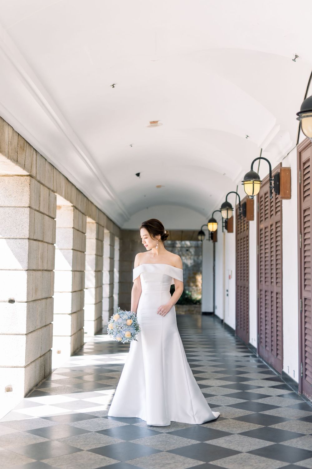 A bride in white dress walks through an elegant checkered hallway with arched ceilings.