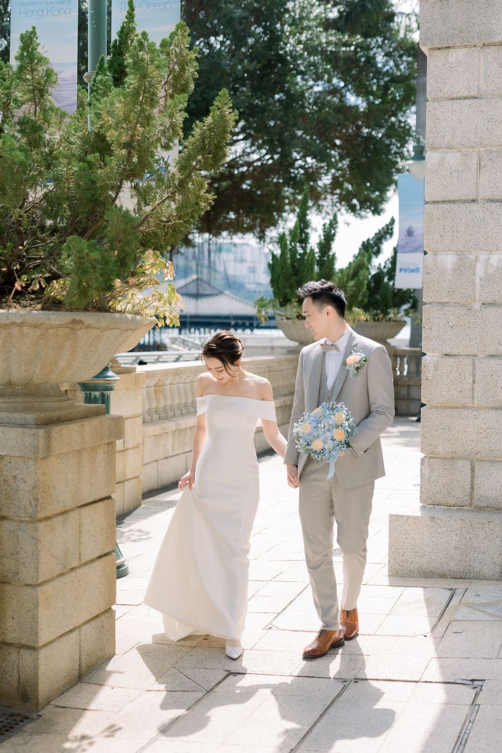 Elegant couple walks along stone terrace walkway with bride holding blue bouquet.