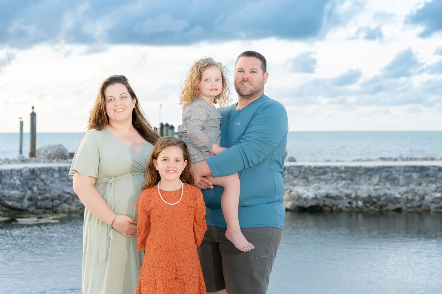 Family standing together on a stone pier overlooking the ocean at sunset.