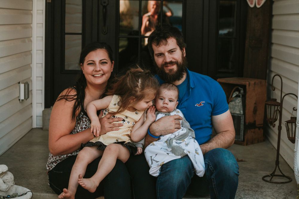 Family of four sitting together on front porch of house.
