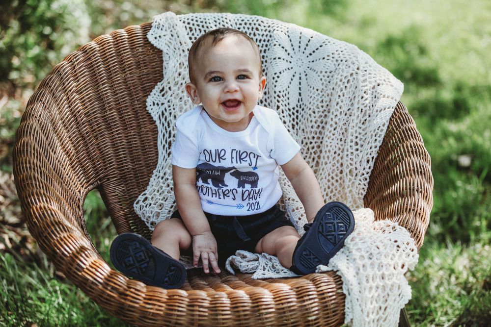 Baby sitting in wicker chair with lace blanket during outdoor portrait session.