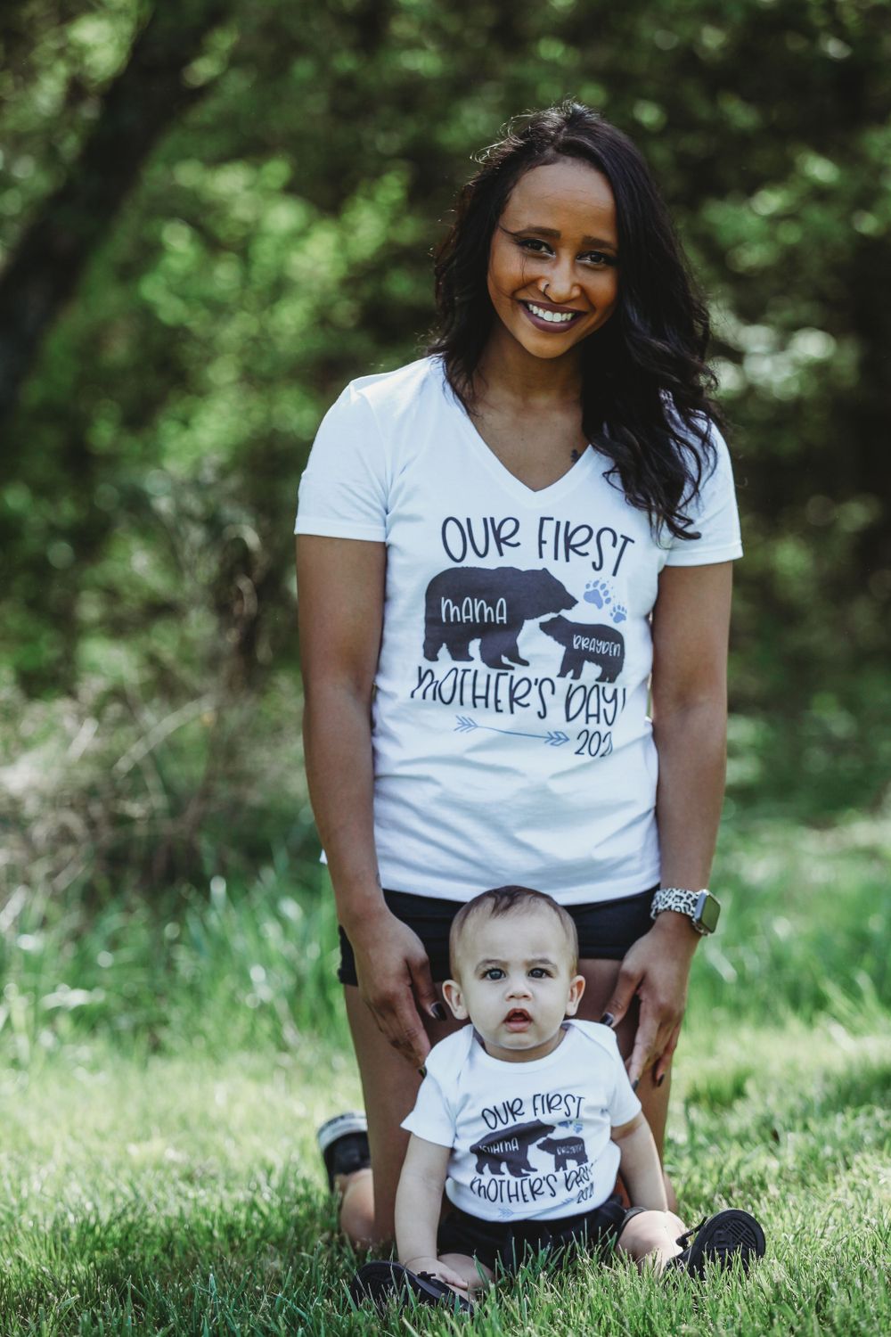 Mother and baby wearing matching graphic t-shirts sitting on grass during outdoor photoshoot.