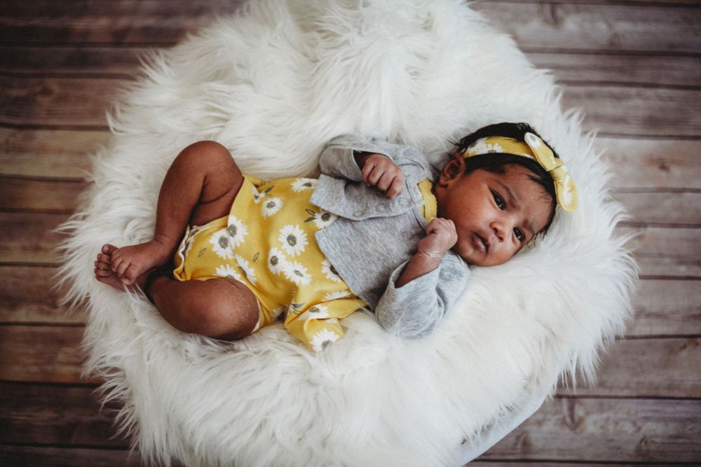 Newborn baby sleeping peacefully on soft white fur blanket against rustic wooden backdrop.