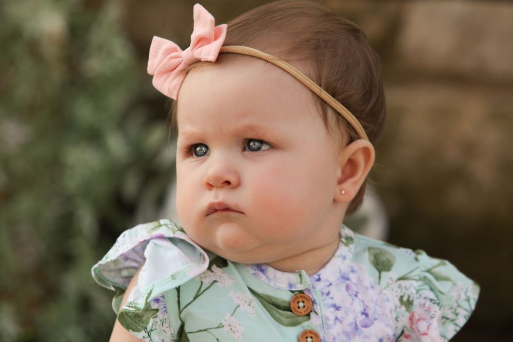 Baby wearing floral dress and pink bow headband looks off into distance.