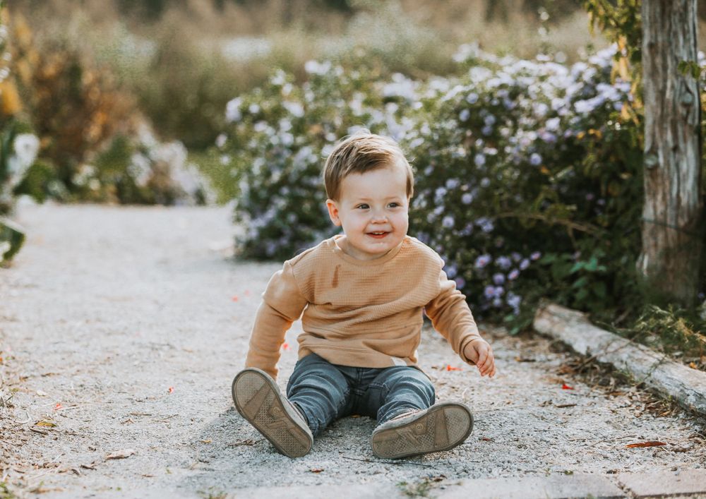 Child playing and crawling on a gravel path during an outdoor photo session.