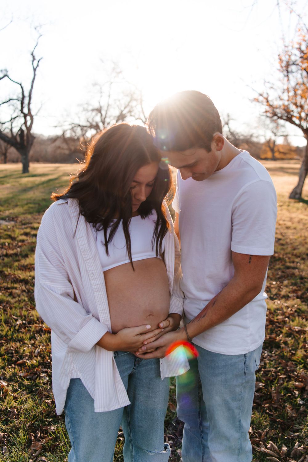 A couple shares an intimate moment during their maternity photoshoot as sunlight creates lens flares.