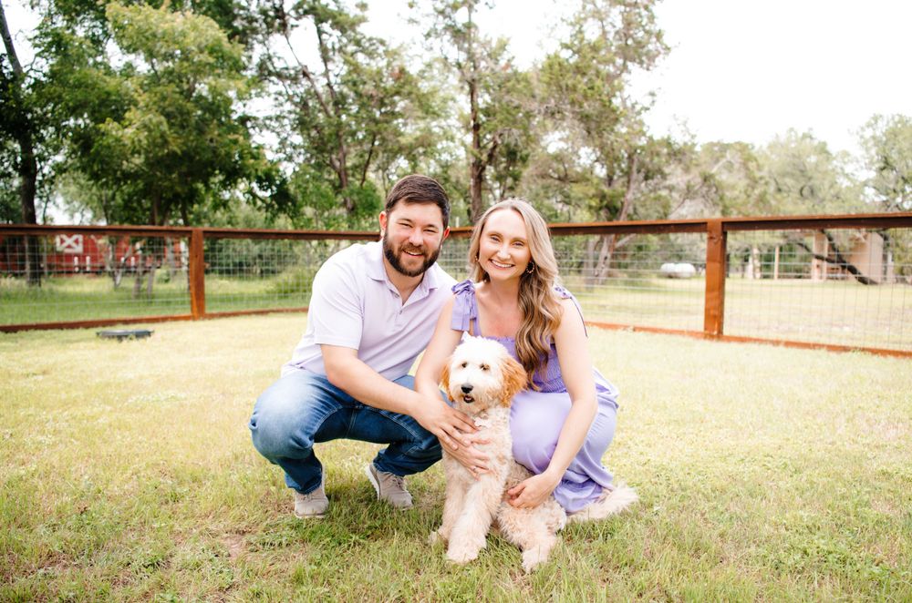 Candid moments captured of couple playing with their dog in grassy field.