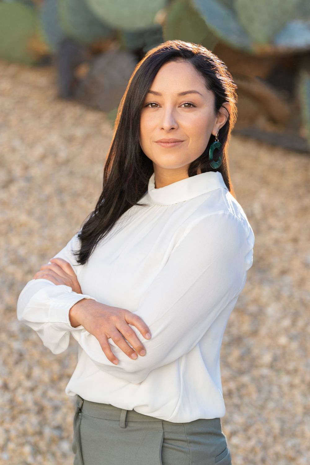 Orange County photographer captures Confident woman in white blouse with arms crossed standing near desert cactus backdrop.
