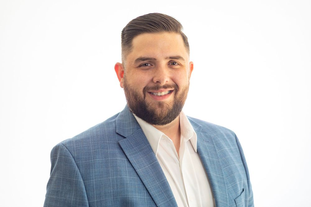 Orange County photographer captures Bearded man in blue blazer smiling against white background professional headshot.