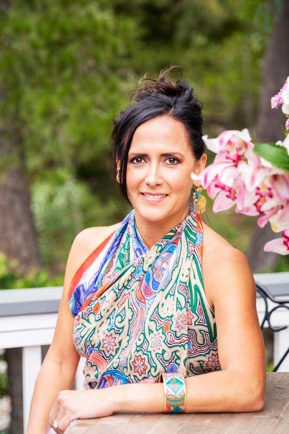 Orange County photographer captures Dark-haired woman in colorful halter top seated outdoors near pink flowers smiling.