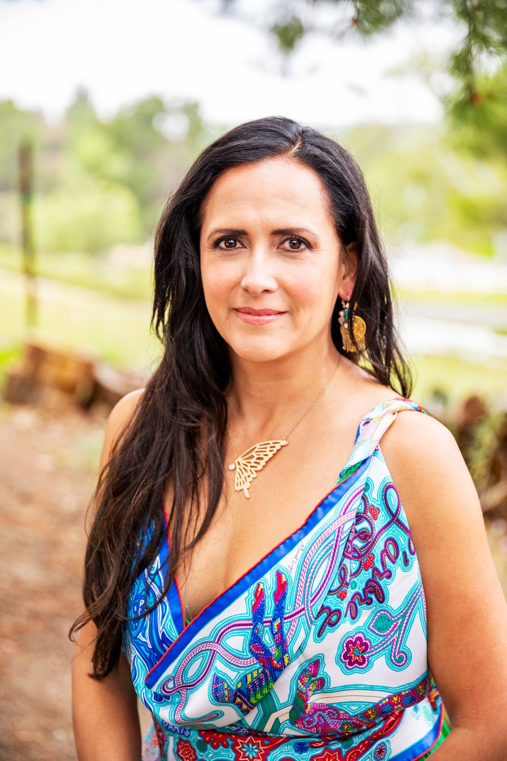 Orange County photographer captures Brunette woman in colorful blue paisley dress with gold necklace posing outdoors.