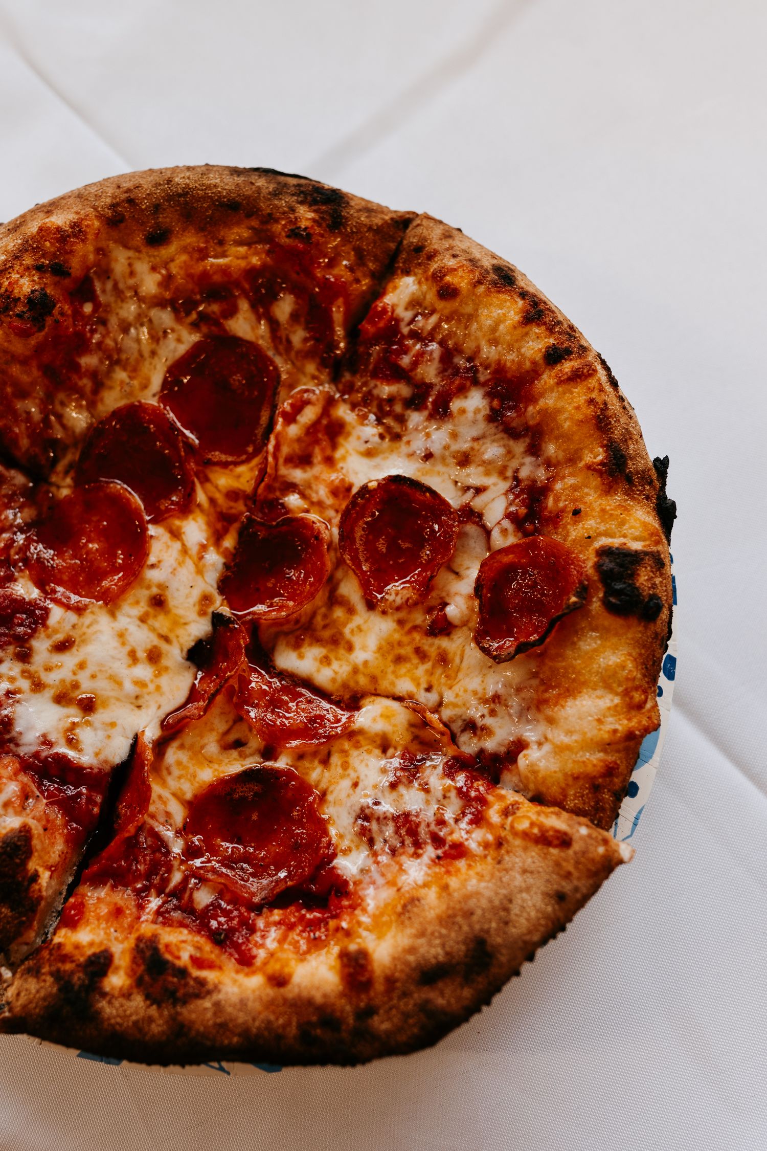 A close-up shot of a wood-fired pepperoni pizza with melted cheese on white background.