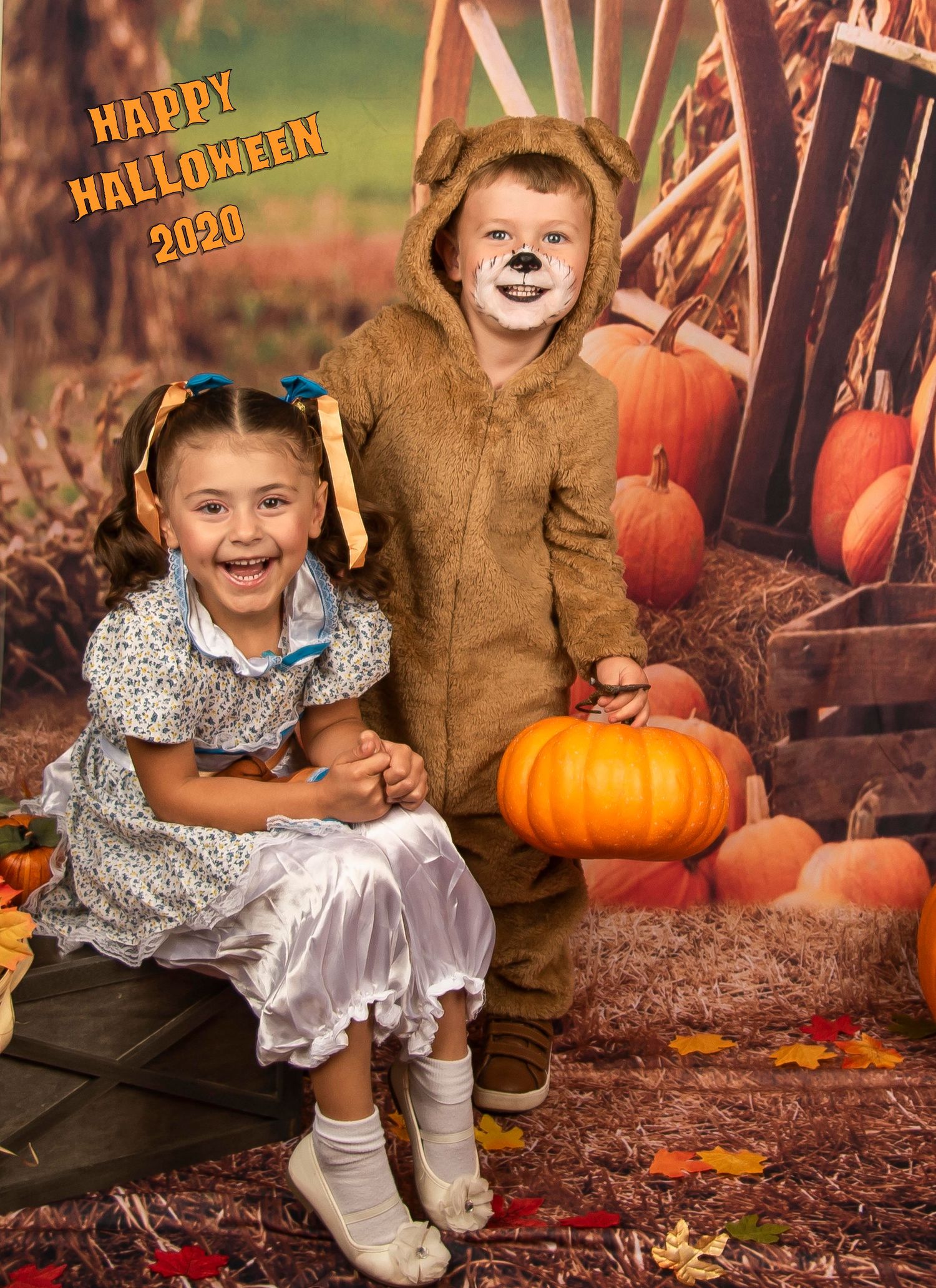Two children in Halloween costumes pose with pumpkins against an autumn backdrop.