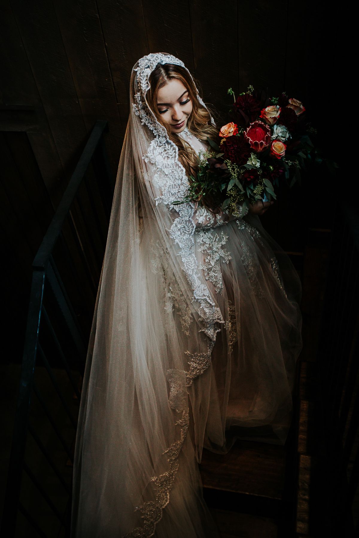 bride on stairwell with long veil looking down holding flowers bouquet