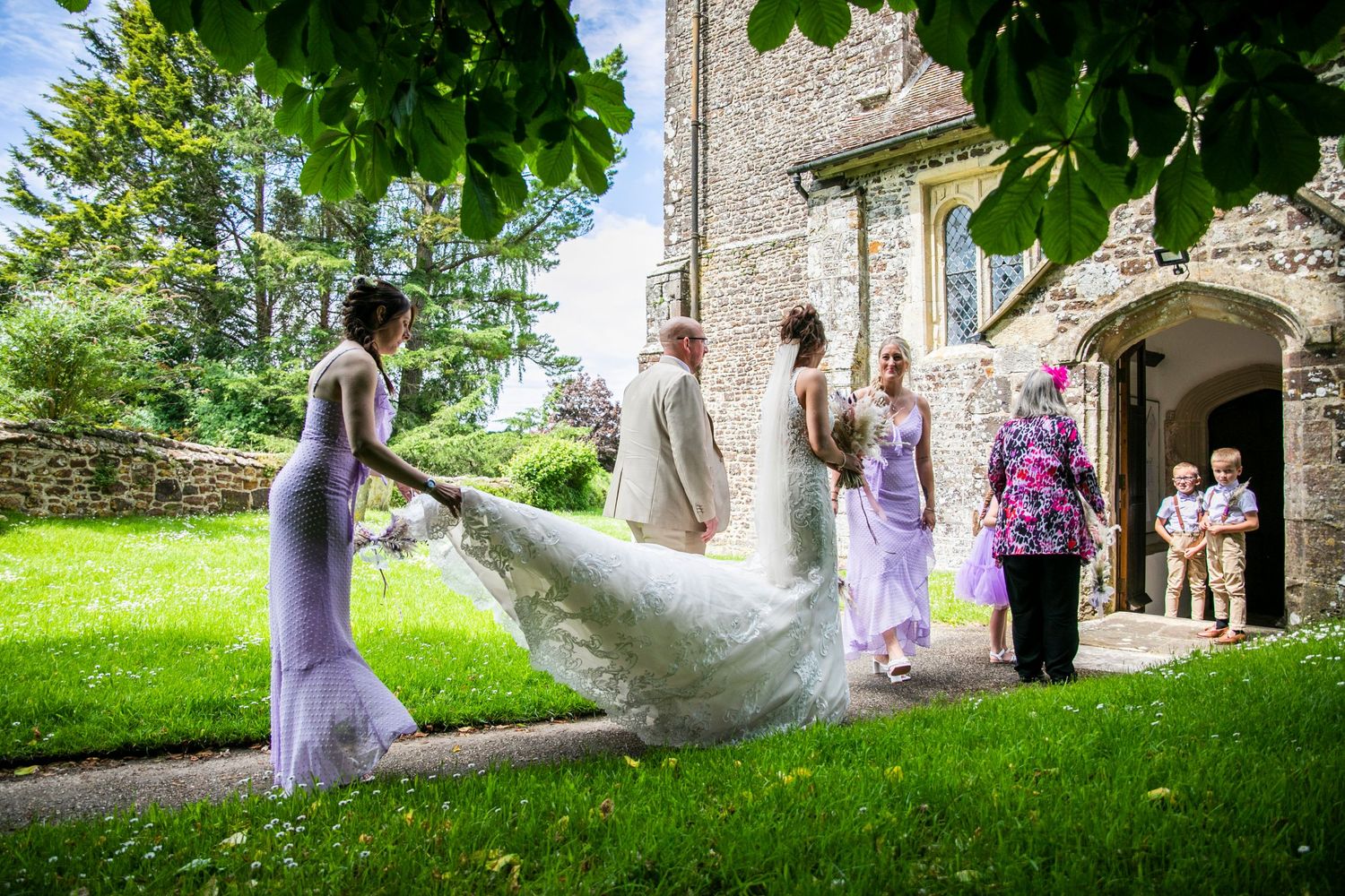 Wedding party takes romantic photos on church grounds with stone architecture and green landscape.