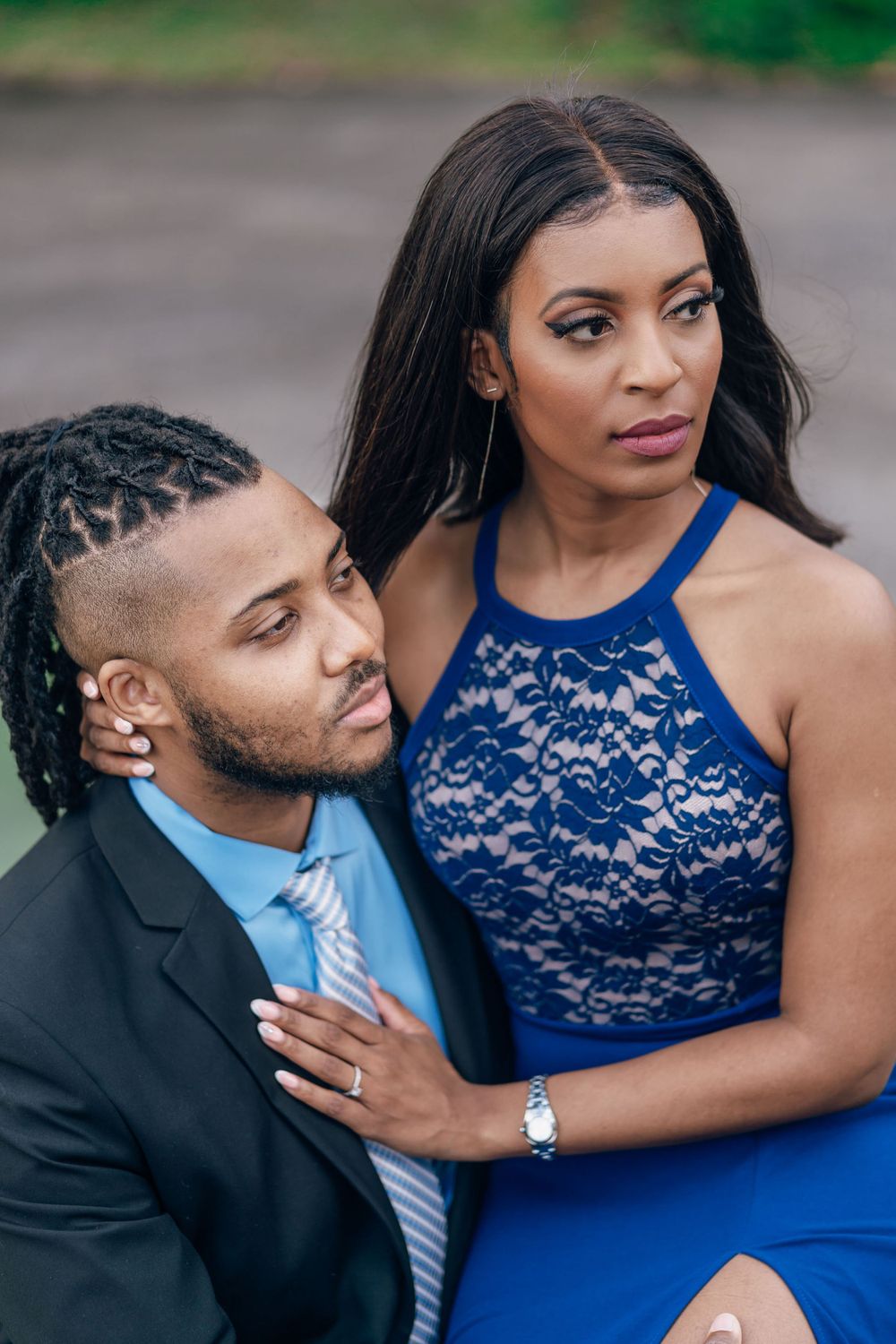 Elegant couple in blue and black formal wear posing for engagement photos outdoors.