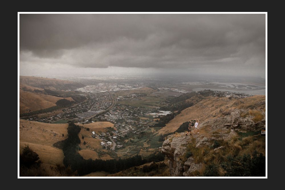 Dramatic aerial view of a city valley surrounded by brown hills under moody storm clouds.