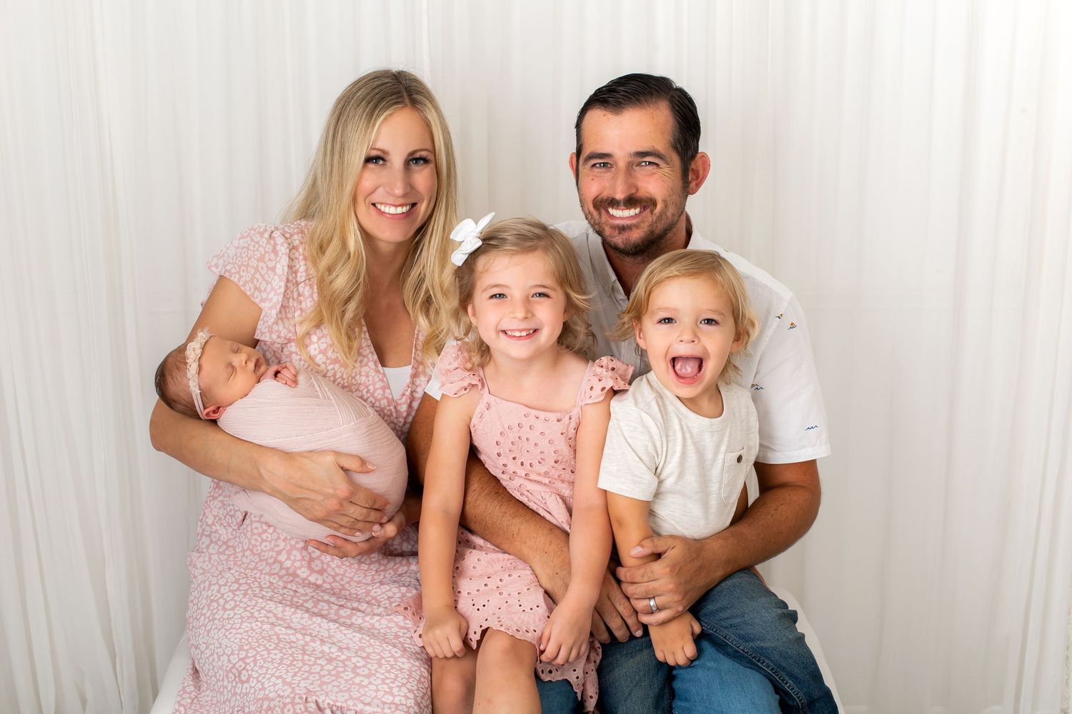 A family with two children sits together for a portrait against a white background.