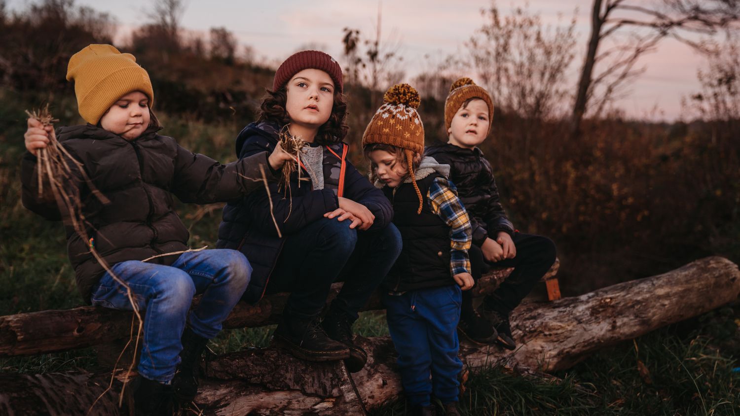 colour image 4 young boys sitting side by side on a log in golden hour light