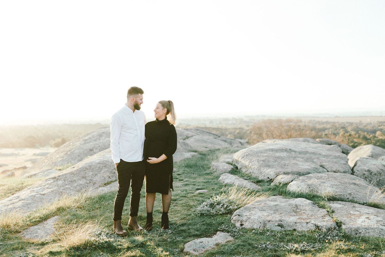 Couple stands together on rocky terrain during golden hour photography session.