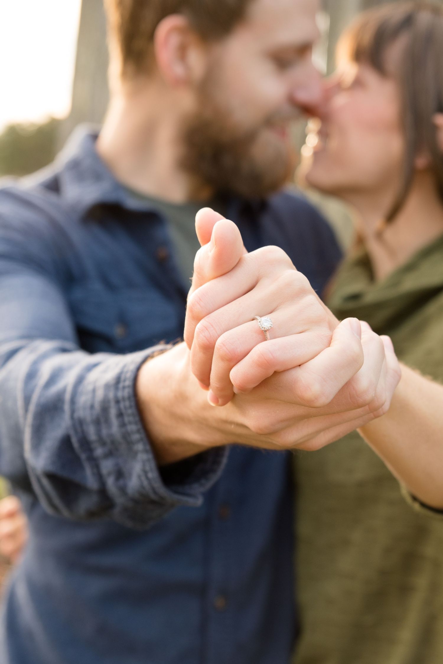 Close up of couple holding hands with engagement ring in focus.