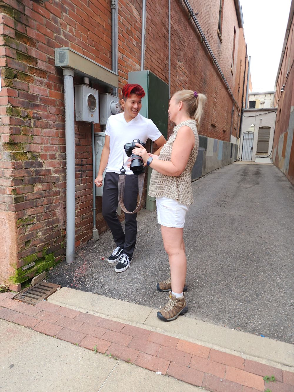 Two people with cameras chat in a narrow brick alleyway.