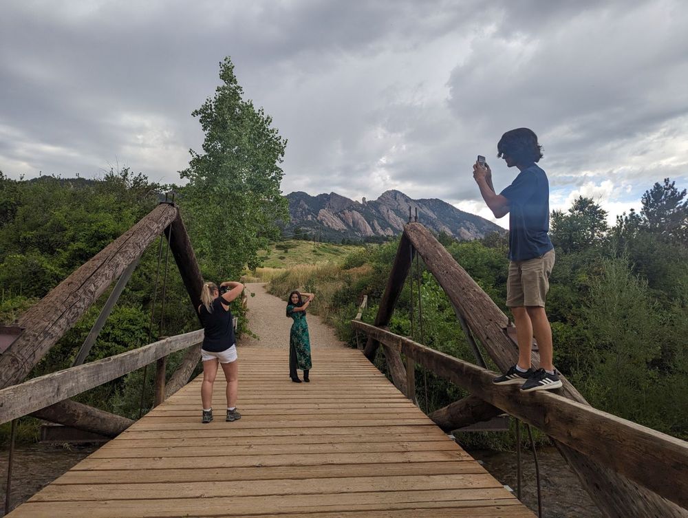 People standing on wooden bridge taking photos of mountain scenery.