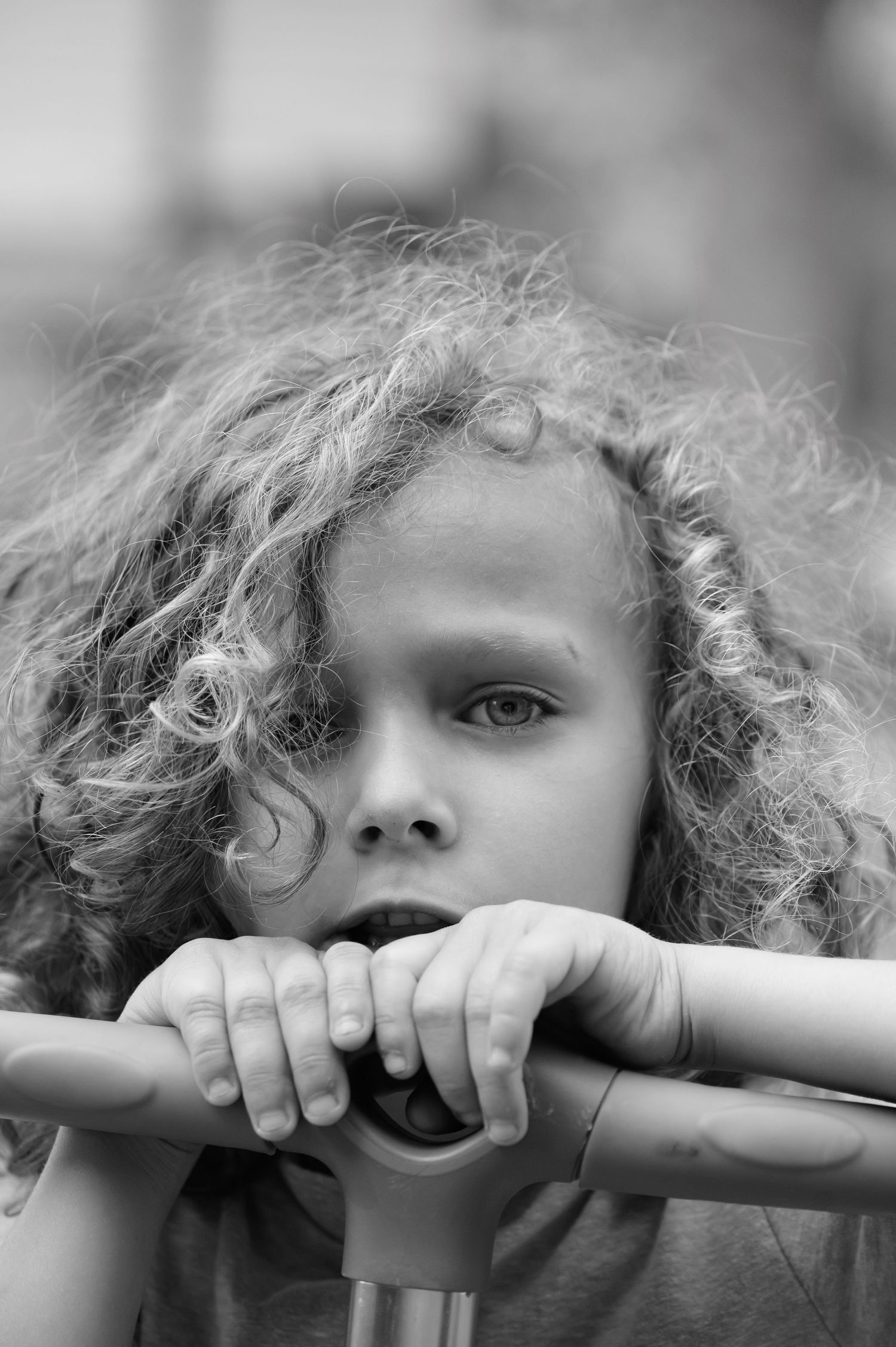 Black and white portrait of a child with curly hair peeking through railings.