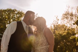 A couple shares an intimate sunset moment in a grassy field with golden light filtering through trees.