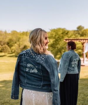 Custom denim jacket over wedding dress shown from behind in outdoor setting.