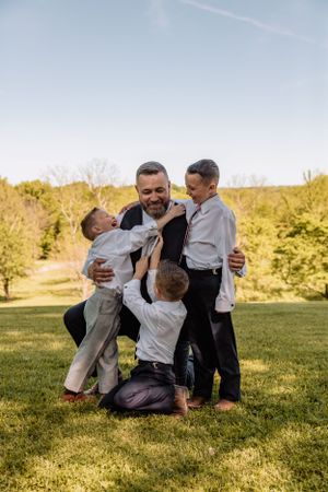 Groomsmen playfully wrestle on the grass during wedding photo session.