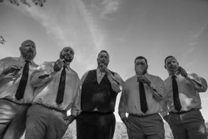 Black and white candid shot of groomsmen laughing together outside.