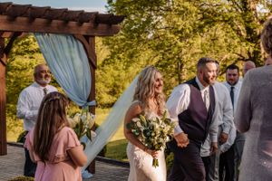 Wedding celebration under wooden pergola with soft blue curtains and natural greenery.
