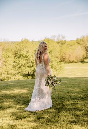 A flowing lace wedding dress catches golden sunlight in an outdoor garden setting.