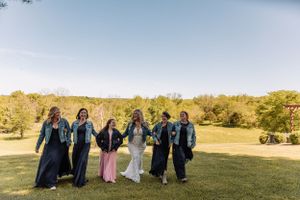 Wedding party in denim jackets and long skirts walking together across a sunny lawn.