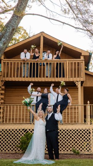 Wedding party poses playfully on wooden deck of rustic cabin venue.