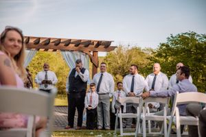 Wedding ceremony setup with white chairs and wooden pergola in an outdoor garden setting at golden hour.