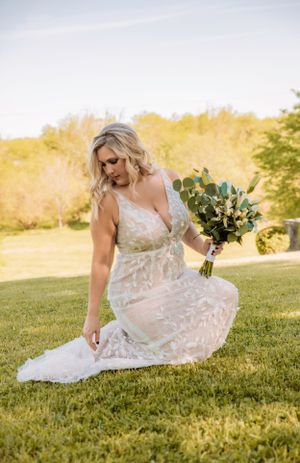 Delicate lace wedding dress billows in the breeze on a sunny hillside.