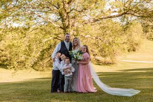 Large wedding party poses for group photos on a grassy hill during golden hour.