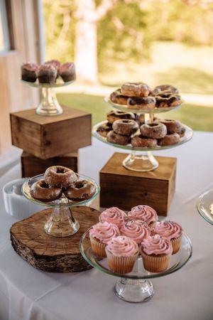 Cupcakes and pastries displayed on wooden crates and glass stands at a wedding dessert table.