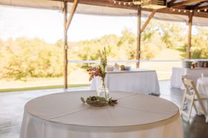 Wedding reception venue with white tables and rustic wooden decor in natural lighting.