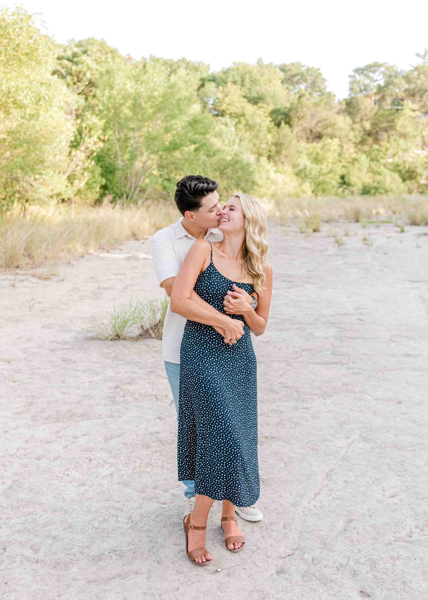 Candid romantic embrace captured along a natural waterfront setting with golden light.