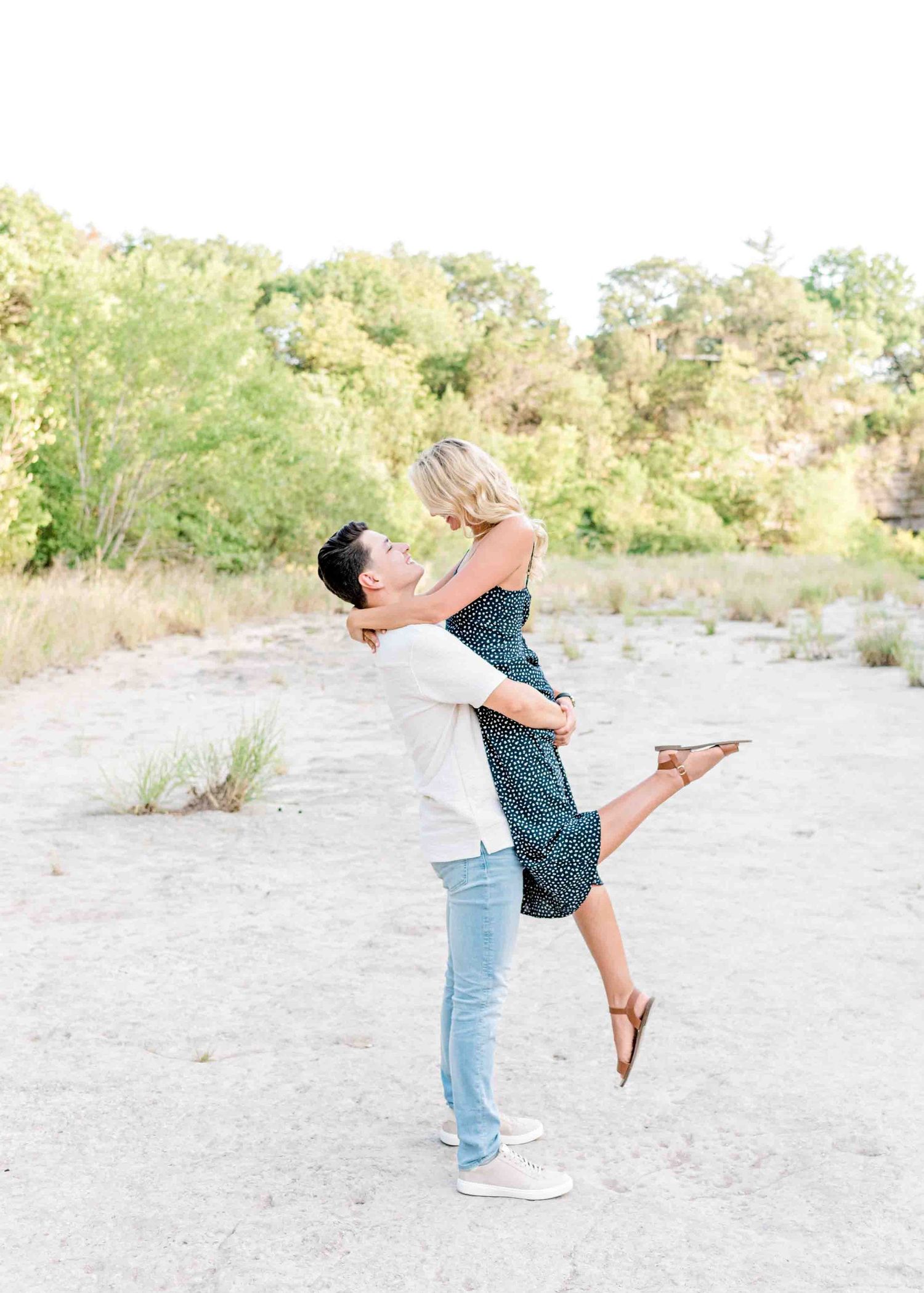 Playful couple moment with lifting pose against a natural outdoor backdrop.