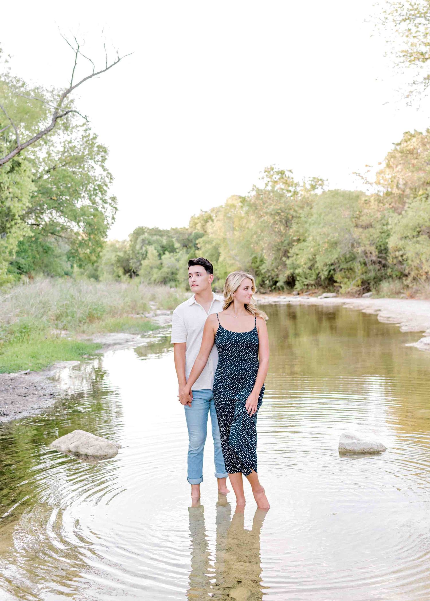 Couple standing together in shallow water with trees and nature in background.