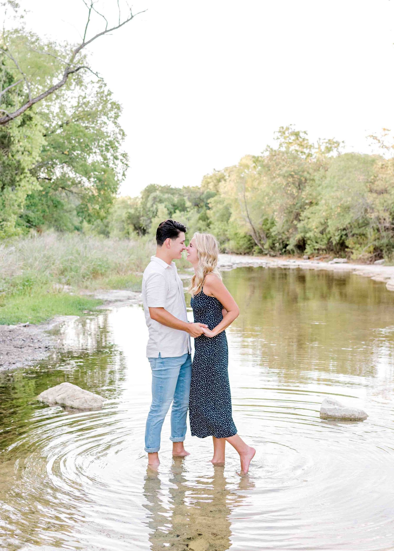 Intimate moment captured of couple standing in rippling water surrounded by greenery.